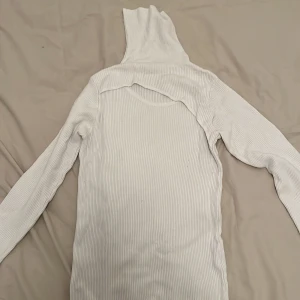 Vit ribbad polotröja - Säljer en stilren vit ribbad polotröja med lång ärm och hög krage. Perfekt för kyligare dagar och kan enkelt matchas med olika outfits. Den är i storlek L men passar även M.