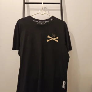 Svart t-shirt med skelettmotiv från Philipp Plein - Cool svart t-shirt från Philipp Plein med ett stort skelettmotiv på baksidan och korsade benknotor med logotyp på framsidan. Helt ny
