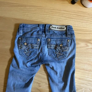 Blå jeans från Rock Revival - Snygga blå jeans från Rock Revival med dekorativa bakfickor och små hål på benen. Säljer pågrund av att de försmå!! Köpte för 600 säljer för 450kr❤️Hålen är lite större kan skicka egen bild!! Pris kan diskuteras 