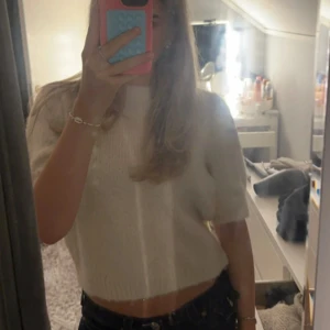 Vit stickad croppad tröja - Säljer en söt vit stickad tröja med korta ärmar och croppad passform. Perfekt för en avslappnad stil. Väldigt liten i storlek så passar även M och S