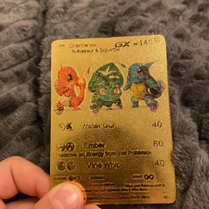Gyllene Pokémon-kort med Charmander, Bulbasaur och Squirtle - Unikt gyllene Pokémon-kort med Charmander, Bulbasaur och Squirtle. Kortet har en glänsande yta och visar de tre klassiska Pokémon-figurerna i färg. Perfekt för samlare eller Pokémon-fans!