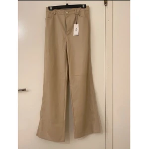 Beige vida byxor - Snygga beige/vitkräm byxor (i läder) med hög midja och vida ben. Perfekta för en stilren look. Byxorna har en klassisk design med knappar och dragkedja framtill. Helt oanvända byxor som fortfarande har prislapp. Väldigt sköna men långa för mig. Den är i storlek 38/M. 