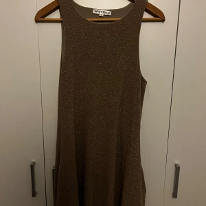 Brun glittrig klänning från MissKoo - Snygg guld klänning från MissKoo med glittrande detaljer. Perfekt för en kväll ute eller en speciell tillställning. Klänningen har en ärmlös design och en elegant passform. Klänningen har även 2 fickor✨⭐️