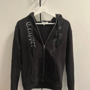 Svart hoodie från Trapper - Snygg svart hoodie från Trapper med dragkedja och coola detaljer i form av glittriga mönster på framsidan. Perfekt för en avslappnad stil. Mitt pris är bara för 610 kronor och priset kan förhandlas vid en snabba affär😁