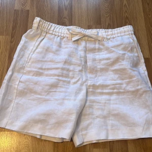 Vita linneshorts från Zara - Snygga vita shorts i linne från Zara med elastisk midja och snörning. Perfekta för varma sommardagar. De har en bakficka och en avslappnad passform. Oanvända utan prislapp, storlek L