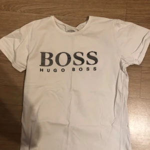 Vit t-shirt från Hugo Boss - Snygg vit t-shirt från Hugo Boss med stort BOSS-tryck på framsidan. Perfekt för en stilren och avslappnad look.