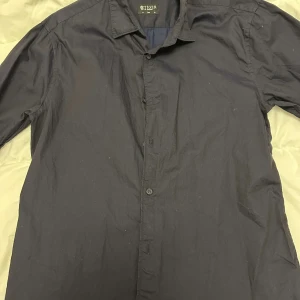 Svart skjorta från Tiger of Sweden - Snygg svart skjorta från Tiger of Sweden med klassisk krage och knappar framtill. Perfekt för en stilren look. Skjortan har långa ärmar och är tillverkad i ett bekvämt material. Storlek 41 SLIM 16 som är M