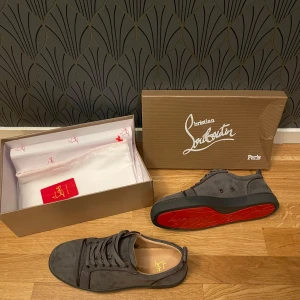Grå sneakers från Christian Louboutin - Snygga grå sneakers från Christian Louboutin med den ikoniska röda sulan. Skorna har en stilren design med snörning och är tillverkade i mocka. Perfekta för en trendig look. Skick 8/10 då de är smått creasade