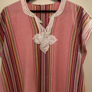 En jätte fin rosa marockanska natt klänning jätte fin har dok använda den några gånger men fin får plats i L,M,S - Säljer en färgglad randig klänning i rosa med inslag av grönt, gult och vitt. Klänningen har ett dekorativt mönster vid halsen och korta ärmar. Perfekt för en avslappnad stil.