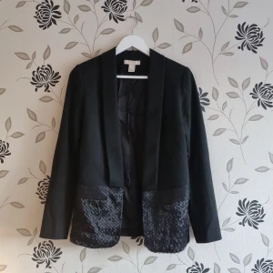 Svart kavaj med glittriga detaljer, Strl: 36/S, H&M,  - Snygg svart kavaj från H&M med glittriga detaljer på fickorna. Perfekt för att ge en extra touch till din outfit. Kavajen har långa ärmar och en klassisk passform.