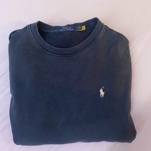 Mörkblå sweatshirt från Polo Ralph Lauren - Säljer en stilren mörkblå sweatshirt från Polo Ralph Lauren med det klassiska logotypen. Tröjan har rund hals och långa ärmar, perfekt för en avslappnad look. Skulle säga att du som vanligtvis är M bör passa perfekt i denna. 