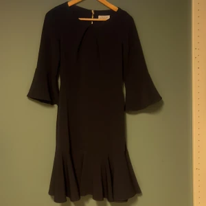 Svart klänning från Closet London - Elegant blå klänning från Closet London med trekvartsärmar och volangdetalj vid fållen. Klänningen har en stilren dragkedja i ryggen och en rund halsringning. Perfekt för en chic look.