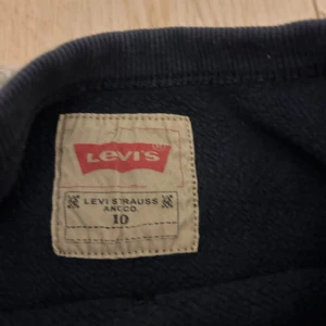 Mörkblå tröja från Levi's - Säljer en mörkblå tröja från Levi's med det klassiska röda logotyptrycket på framsidan. Tröjan har långa ärmar och en rund halsringning. Perfekt för en avslappnad stil. Str 10 år