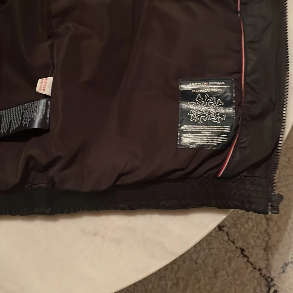Snygg svart dunväst från Tommy Hilfiger med dragkedja och hög krage. Västen har märkets logga på bröstet och ett stort tryck på ryggen. Perfekt för kyliga dagar. Väldigt bra skick och knappt använd! OBS frakt börjar på 68kkr. Takit.