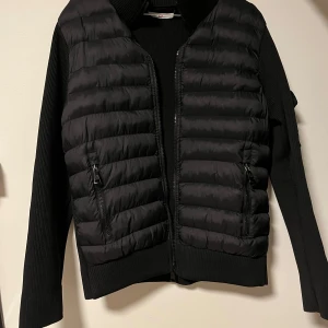 Svart cardigan från Moncler - Snygg svart cardigan från Moncler med ribbade ärmar och dragkedja framtill. Jackan har två praktiska fickor med dragkedja och en broderad Moncler-logga på ärmen.                              Köparen står för frakten💘