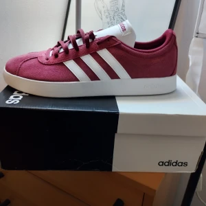 Adidas VL Court 2.0 i vinrött - Snygga Adidas VL Court 2.0 sneakers i vinrött med vita detaljer. Skorna har en klassisk design med tre vita ränder på sidan och snörning framtill. Perfekta för en stilren och sportig look.