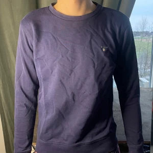 Mörkblå långärmad tröja från Gant - Säljer en stilren mörkblå långärmad tröja från Gant. Tröjan har en rund halsringning och ett diskret broderat märke på bröstet. 