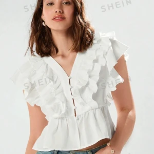 Vit blus med volanger - Säljer en superfin vit blus från SHEIN med volanger och v-ringning. Den har en luftig och somrig stil med korta ärmar och en lätt croppad passform. Perfekt för både vardag och fest!