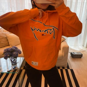 Tommy hillfiger hoodie - Säljer en snygg orange hoodie från Tommy hillfiger. Den har en stor logga i blått och vitt på framsidan och en praktisk magficka. Perfekt för en casual look eller att mysa i hemma. 