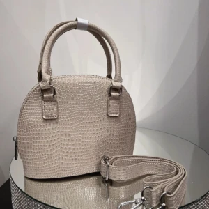 Beige handväska med krokodilmönster - Snygg beige handväska i syntetmaterial med krokodilmönster. Den har en avtagbar axelrem och dragkedja upptill. Perfekt för både vardag och fest!