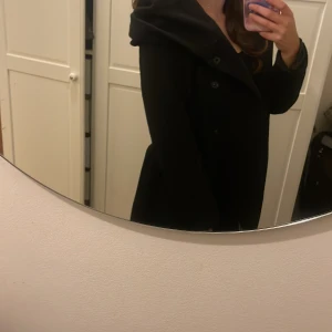 Svart kappa med huva - Säljer en stilren svart kappa med huva. Perfekt för höst och vinter. Den har långa ärmar och knappar framtill. Passar både till vardags och festliga tillfällen. Superbekväm och håller dig varm!