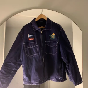 Mörkblå jacka med broderade detaljer - Säljer en snygg mörkblå jacka från Zara med coola broderade detaljer på bröstet. Jackan har en dragkedja framtill och två stora fickor. Perfekt för höst och vår! Passar både till vardags och lite mer avslappnade tillfällen. 🧥✨