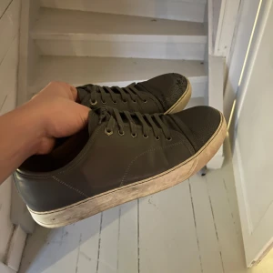 Gråa sneakers från Lanvin - Säljer ett par gråa sneakers från Lanvin i bra skick. De har en stilren design med snörning och en vit sula som har lite slitage. Perfekta för vardagsbruk och passar till de flesta outfits. Skostorlek 44