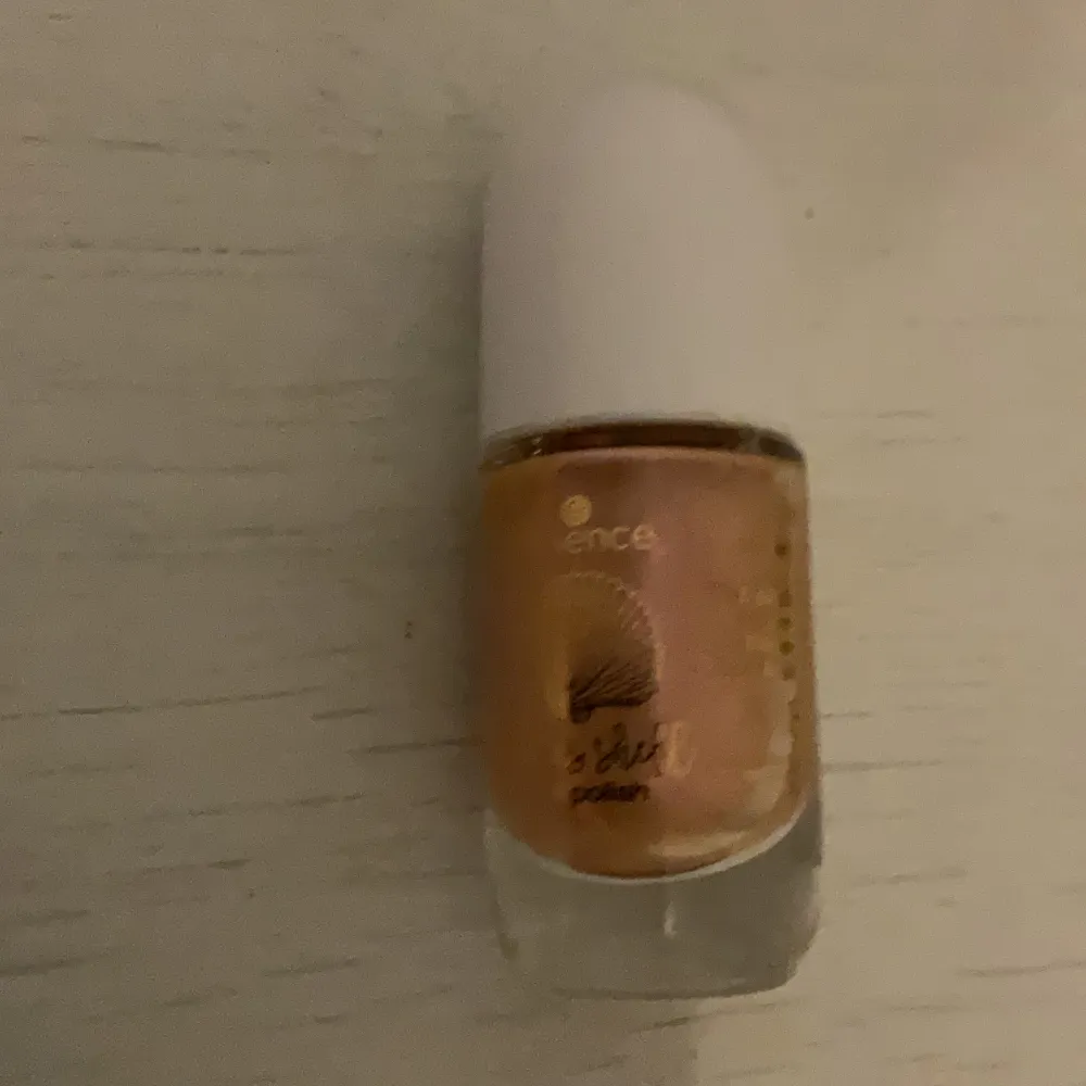 Säljer ett superfint nagellack från Essence i en skimrande guldig nyans. Perfekt för att ge dina naglar en glittrig och elegant look. Flaskan är liten och smidig med en vit kork. Passar både till vardags och fest!. Skönhet.