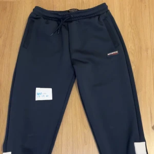 Mörkblåa mjukisbyxor från McKenzie - Säljer ett par mörkblåa mjukisbyxor från McKenzie i bra skick. De har en elastisk midja med snörning och vita detaljer vid bensluten. Perfekta för en avslappnad dag eller träning. 