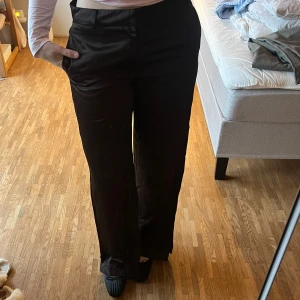 Svarta byxor från Zara - Säljer ett par mörkbruna byxor från Zara i storlek S. är tillverkade i ett glansigt material. Perfekta för både vardag och fest! 🖤