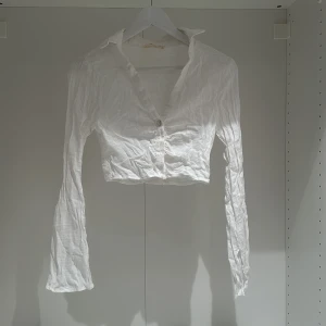 Vit croppad skjorta från Pull&Bear - Säljer en superfin vit croppad skjorta från Pull&Bear. Den har långa ärmar och knappar framtill. Perfekt för sommaren eller våren, och kan stylas både upp och ner. Skjortan är i bra skick och gjord av ett lätt och bekvämt material.