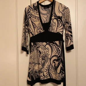 Mönstrad Blus från Kapphal - Snygg mönstrad blus från kapphal  i svart och beige. Den har trekvartsärmar och ett unikt mönster som verkligen sticker ut. Perfekt för både vardag och fest! Blusen knytes bak och är gjord i ett mjukt och bekvämt material.