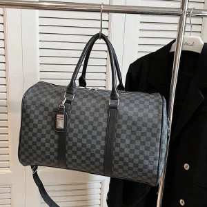 Rutig weekendväska i syntet - Snygg och praktisk rutig weekendväska i grått och svart. Perfekt för kortare resor eller som gymväska. Väskan har en dragkedja upptill och en justerbar axelrem för bekväm bärning. Den är rymlig och stilren, vilket gör den till ett mångsidigt val för alla tillfällen.