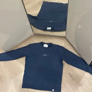 Mörkblå sweatshirt från Les Deux - Säljer en snygg mörkblå sweatshirt från Les Deux. Den har en klassisk design med rund hals och ribbade muddar. Perfekt för både vardag och avslappnade tillfällen. Märket är broderat på bröstet för en stilren look.