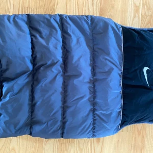 Blå dunväst från Nike - Säljer en snygg blå dunväst från Nike. Den har en dragkedja framtill och två praktiska fickor. Perfekt för kyliga dagar när du vill hålla värmen utan att bära en jacka. Västen är i mycket bra skick och passar perfekt för höst och vår.