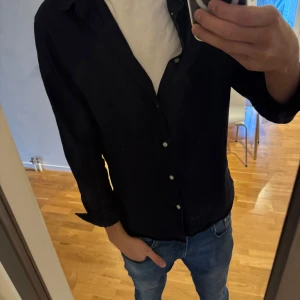 Svart linne skjorta från H&M - Säljer en stilren svart linne skjorta från H&M i storlek M. Skjortan är långärmad och har knappar framtill. Perfekt för både vardag och festliga tillfällen. Materialet känns bekvämt och passar bra till jeans eller kostymbyxor. Ett måste i garderoben! 🖤