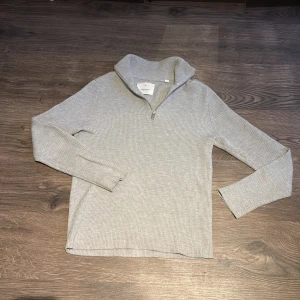 Grå ribbad tröja från Jack & Jones - Säljer en stilren grå ribbad tröja från Jack & Jones. Den har en dragkedja vid halsen och långa ärmar, perfekt för både höst och vinter. Tröjan är i mycket bra skick och passar till både vardag och lite finare tillfällen. Skön och enkel att matcha med andra plagg!