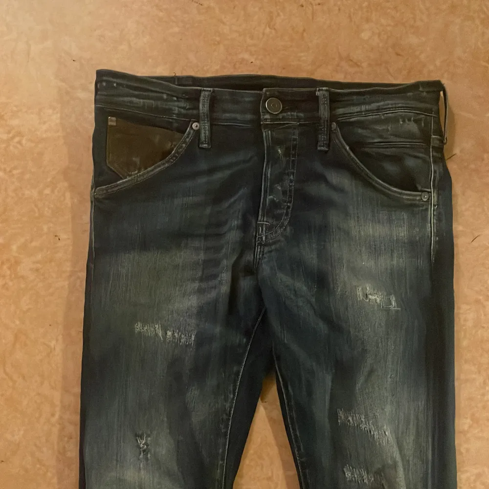 Säljer ett par mörkblå jeans i bra skick med coola slitningar för en avslappnad grisch look. Slim fit killar . Jeans & Byxor.