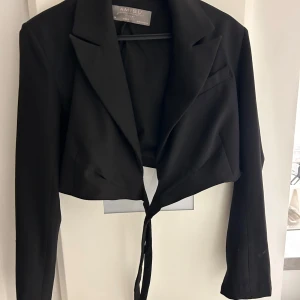 Svart croppad kavaj  - Säljer en snygg svart croppad kavaj. Den har långa ärmar och knytband i midjan. Perfekt för både fest och vardag.🖤