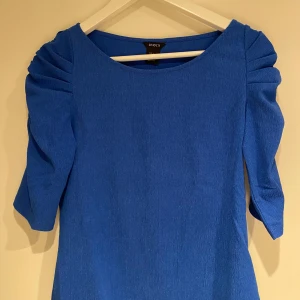 Klarblå blus  från Lindex - Klarblå blus med volangärmar som är trekvartslånga. 95% polyester och 5% elastan, vilket ger en skön stretchig passform. 