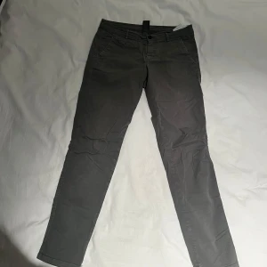 Grå byxor från Dondup - Säljer ett par stilrena grå byxor från Dondup i storlek 14Y. De har en klassisk design med knappar och är perfekta för både vardag och fest. Materialet känns slitstarkt och bekvämt. Passar bra till höst- och vårsäsongen. Perfekt för dig som vill ha en snygg och mångsidig byxa!