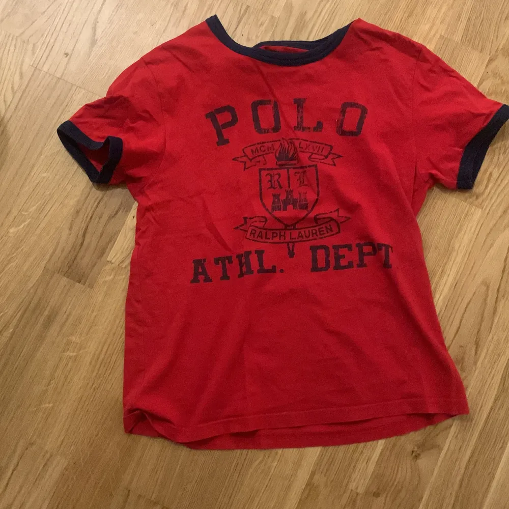 Säljer en snygg röd t-shirt från Ralph Lauren med mörkblå text och detaljer. Den har en klassisk passform och är perfekt för vardagsbruk. Materialet känns mjukt och skönt mot huden. Perfekt för sommardagar eller avslappnade tillfällen. 🏷️. T-shirts.