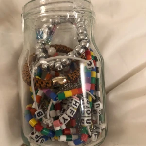 mystery jewelry jar - En samling av färgglada armband i en glasburk. Armbanden har olika färger och mönster, inklusive bokstavspärlor och silverfärgade detaljer. Perfekt för att mixa och matcha till olika outfits.