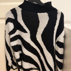 Zebramönstrad stickad tröja från Estee Brown - Snygg zebramönstrad stickad tröja från Estee Brown i svart och vit. Tröjan har en hög krage och långa ärmar, perfekt för att hålla sig varm och trendig. Ett måste för garderoben!