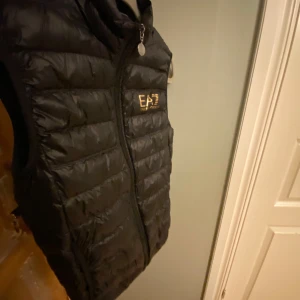 Svart dunväst från Emporio Armani - Snygg svart dunväst från EA7 med dragkedja framtill. Har använt den cirka 5 gånger. Den är köpt från boozt för 900kr på rabatt. Priset är diskuterbart. Du kan komma och prova och om man inte vill ha den efter man har provat så är det ok.