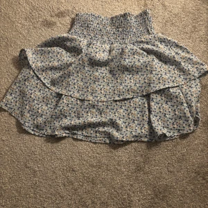 Blommig kjol med volang - Charmig blommig kjol med volangdetaljer och elastisk midja. Perfekt för en somrig look med sitt lätta och luftiga material. Den har en söt och lekfull design som passar bra till olika tillfällen.