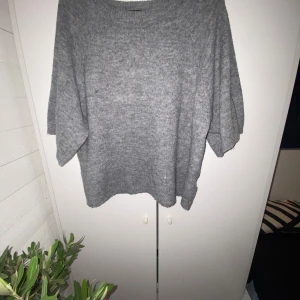 Grå stickad tröja från 157 - Mysig grå stickad tröja från 157 i storlek XS. Perfekt för hemma kvällar med sin bekväma passform och luftiga material. Tröjan har halv långa ärmar och en klassisk rund halsringning. Användning syns då hela varan är lite nopprig, men det funkar🙃