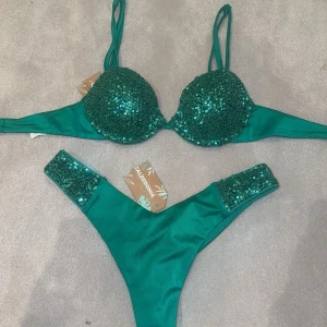 Grön bikini med paljetter - Säljer en emeraldgrön bikini från Calzedonia med glittrande paljetter på både överdel och underdel. ALDRIG ANVÄNDA MED PRISLAPPEN KVAR! 