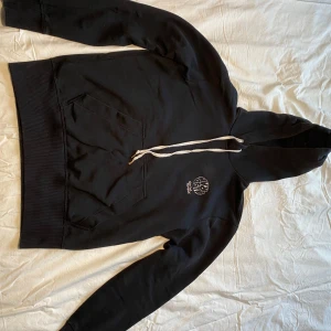 Svart hoodie från G-Star RAW - Säljer en svart hoodie från G-Star RAW med en broderad logga på bröstet. Den har en klassisk känguruficka och justerbar huva med snören. Perfekt för en avslappnad stil.