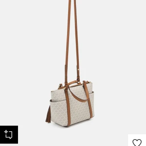 Beige och brun axelväska från Michael Kors - Original pris 3000kr. Snygg axelväska från Michael Kors i beige med bruna detaljer och logotypmönster. Väskan har en justerbar axelrem och handtag, samt en dekorativ tofs. Perfekt för att bära dina dagliga nödvändigheter med stil.